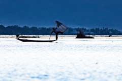 Ein Einbeinfischer mit Rundnetz nach Sonnenuntergang am Inle-See in Myanmar